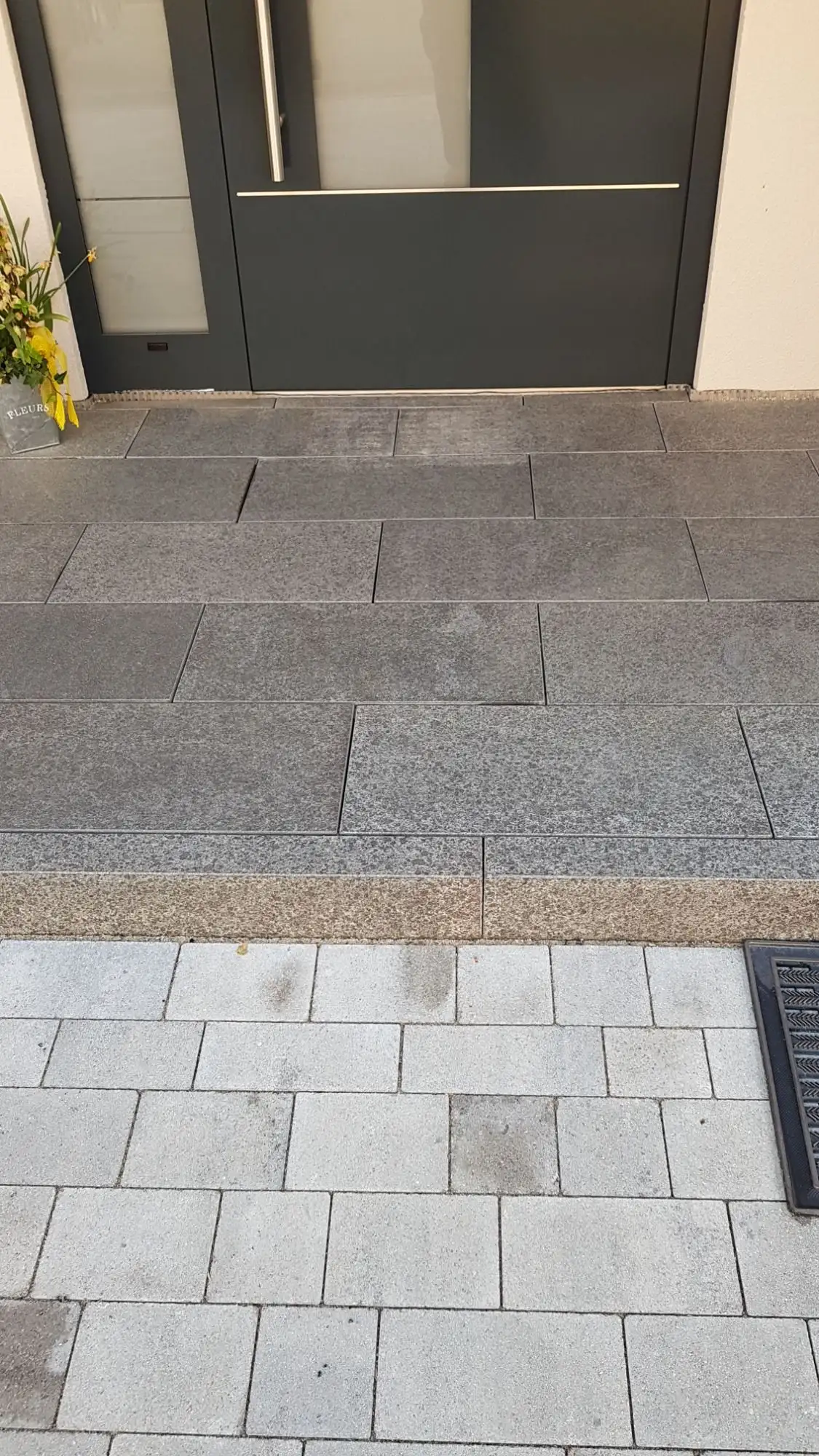 Hauseingang mit dunklen Platten vor der Haustür, davor helles Pflaster