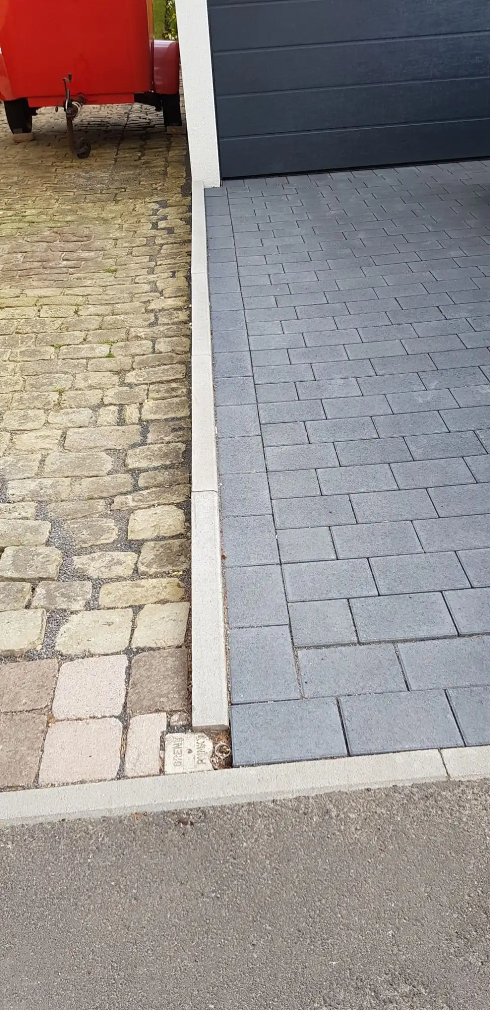 Neuer Streifen aus grauem Betonpflaster neben altem Pflaster vor einer Garage