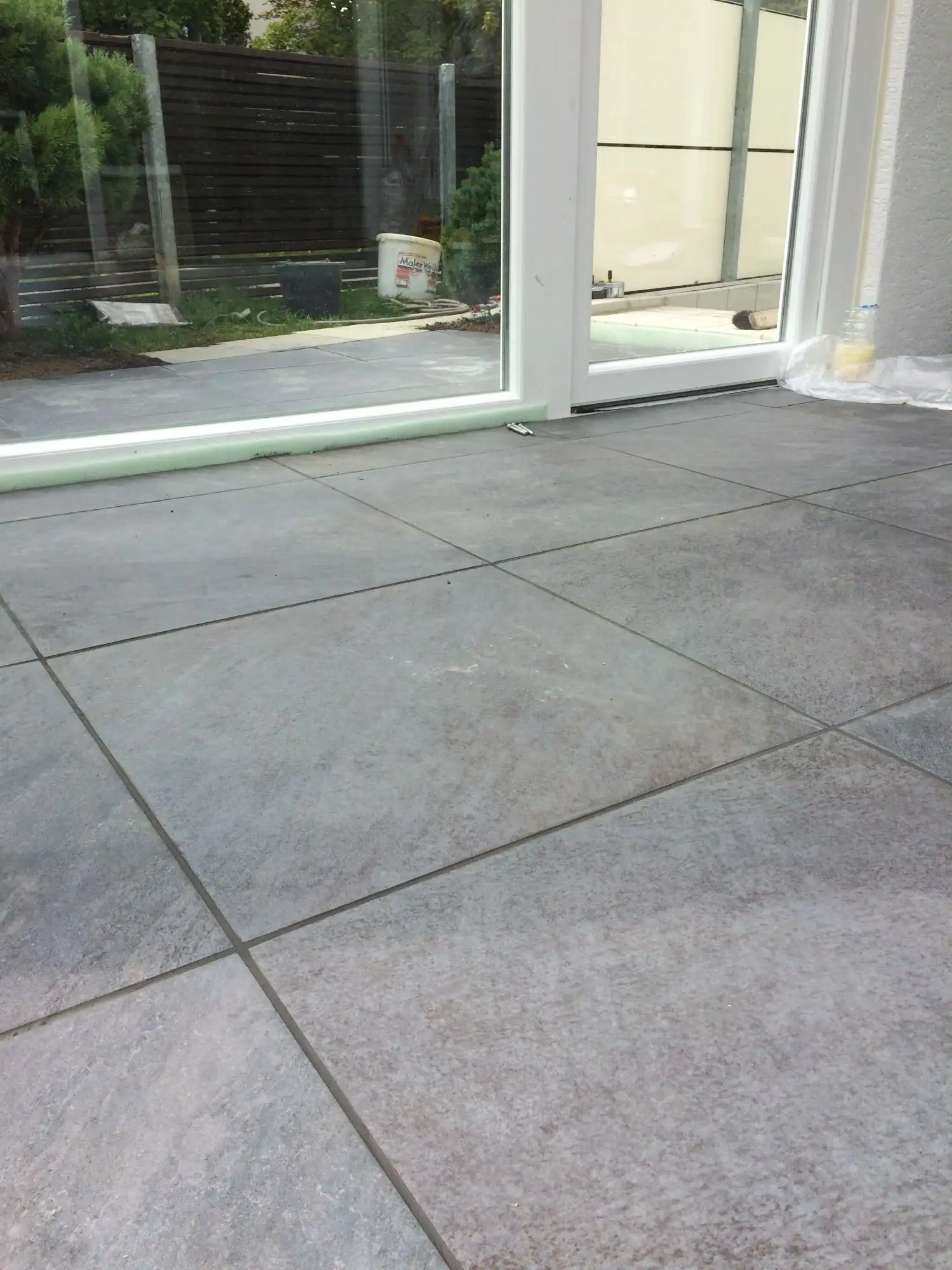 Terrasse aus großen grauen Feinsteinzeug-Platten vor einer Glasfront