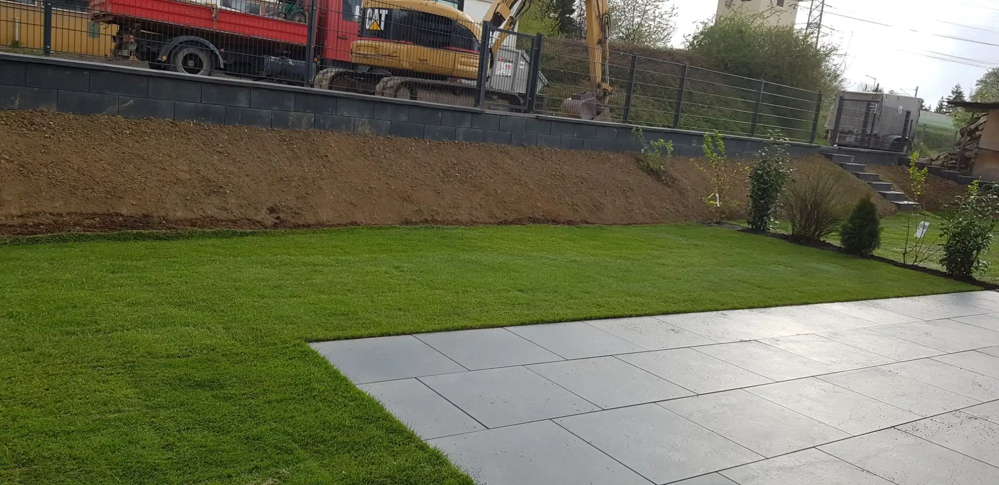 Terrasse aus dunklen Großformatplatten mit angrenzendem neuem Rasen