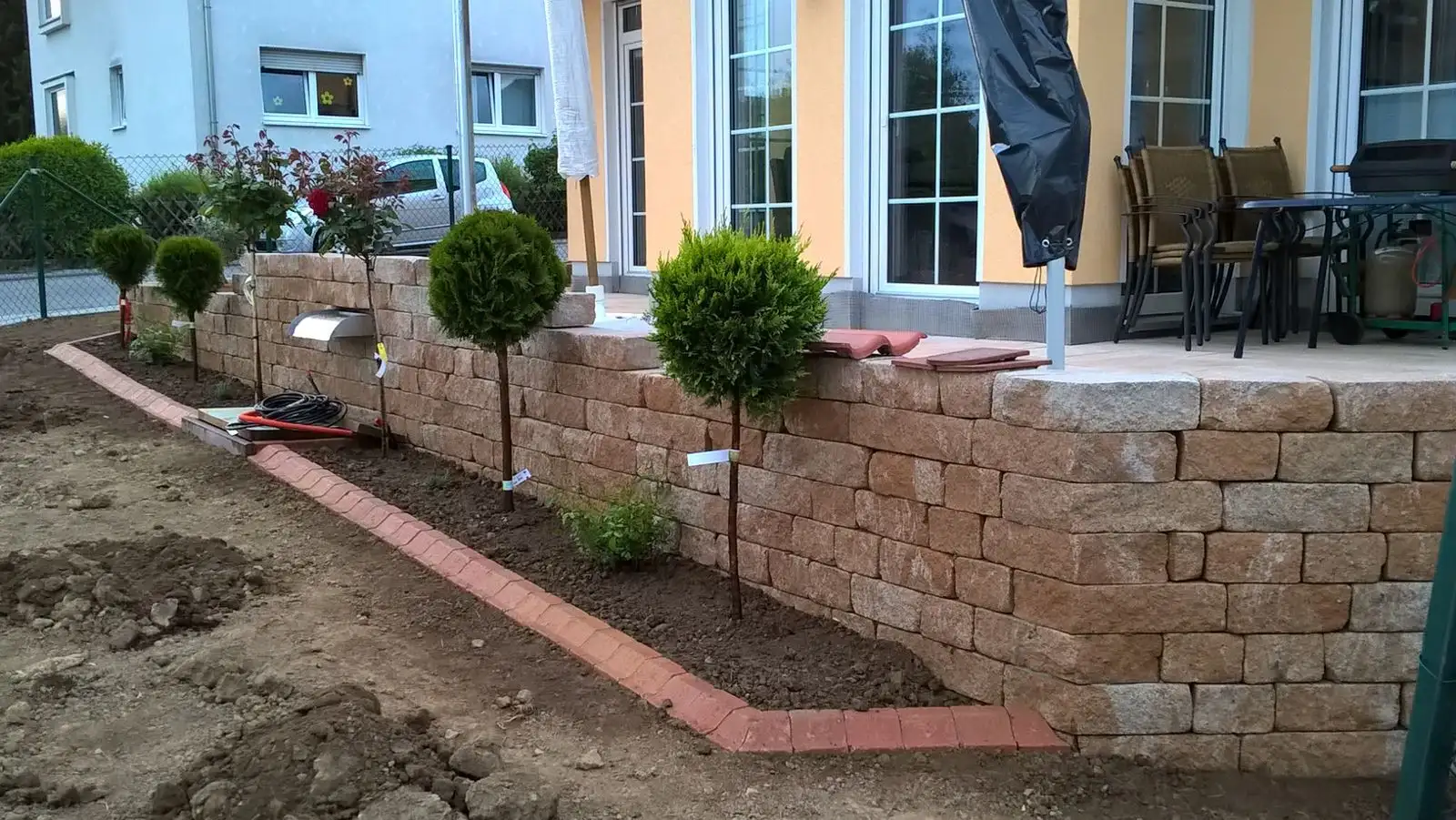 Terrasse mit Natursteinmauer, Kugelbäumchen und frisch angelegtem Beet