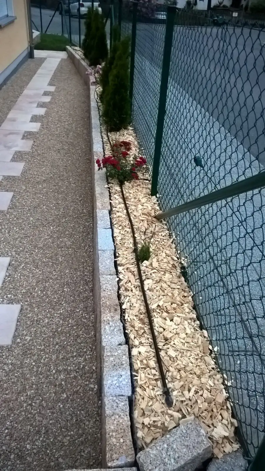 Schmaler Weg aus Waschbeton mit Kiesstreifen entlang eines Zauns