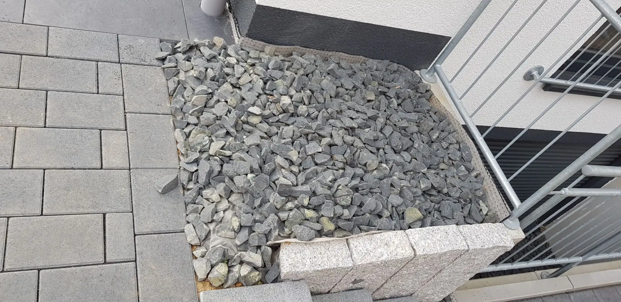 Edelstahl-Geländer an einer Außentreppe, daneben ein Schotterbeet in Steinkante